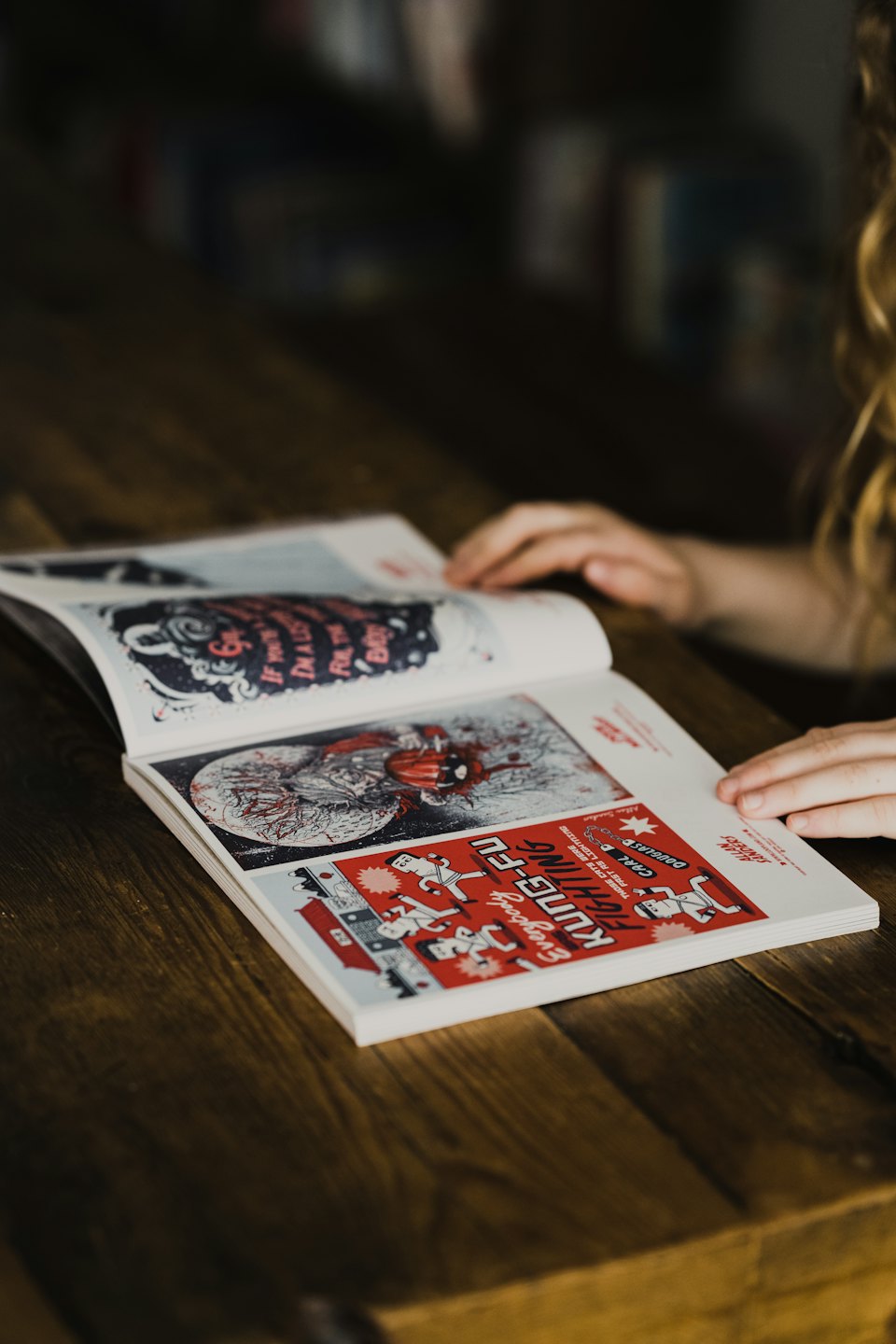 Hands turning pages of an open magazine on a wooden table.