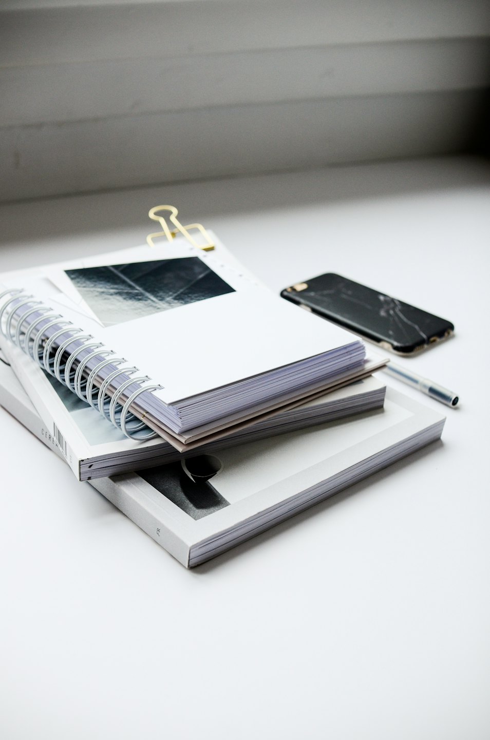 Notebooks and a cracked smartphone on a white desk.